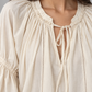 Blusa panna con scollo arricciato e laccetti, lunghe maniche morbide – dettaglio su modella
