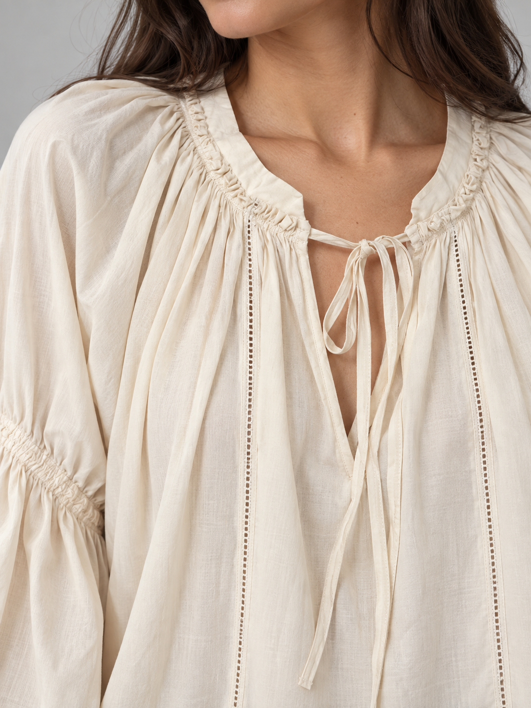 Blusa panna con scollo arricciato e laccetti, lunghe maniche morbide – dettaglio su modella