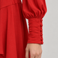 Abito Pinko rosso con scollo incrociato e polsini arricciati — dettaglio su modella (immagine generata con AI)