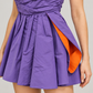 Abito Pinko viola a fascia con dettaglio arancio — dettaglio su modella (immagine generata con AI)